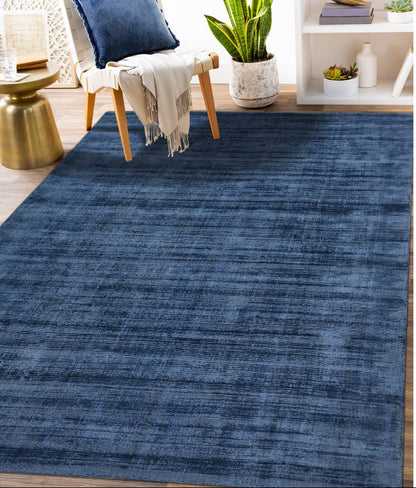 Blue area rug in a living room setting with a chair, table, and plants.