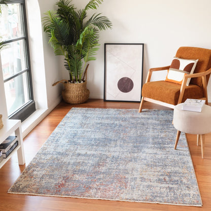Living room with a blue patterned rug, orange armchair, and a plant near a window.