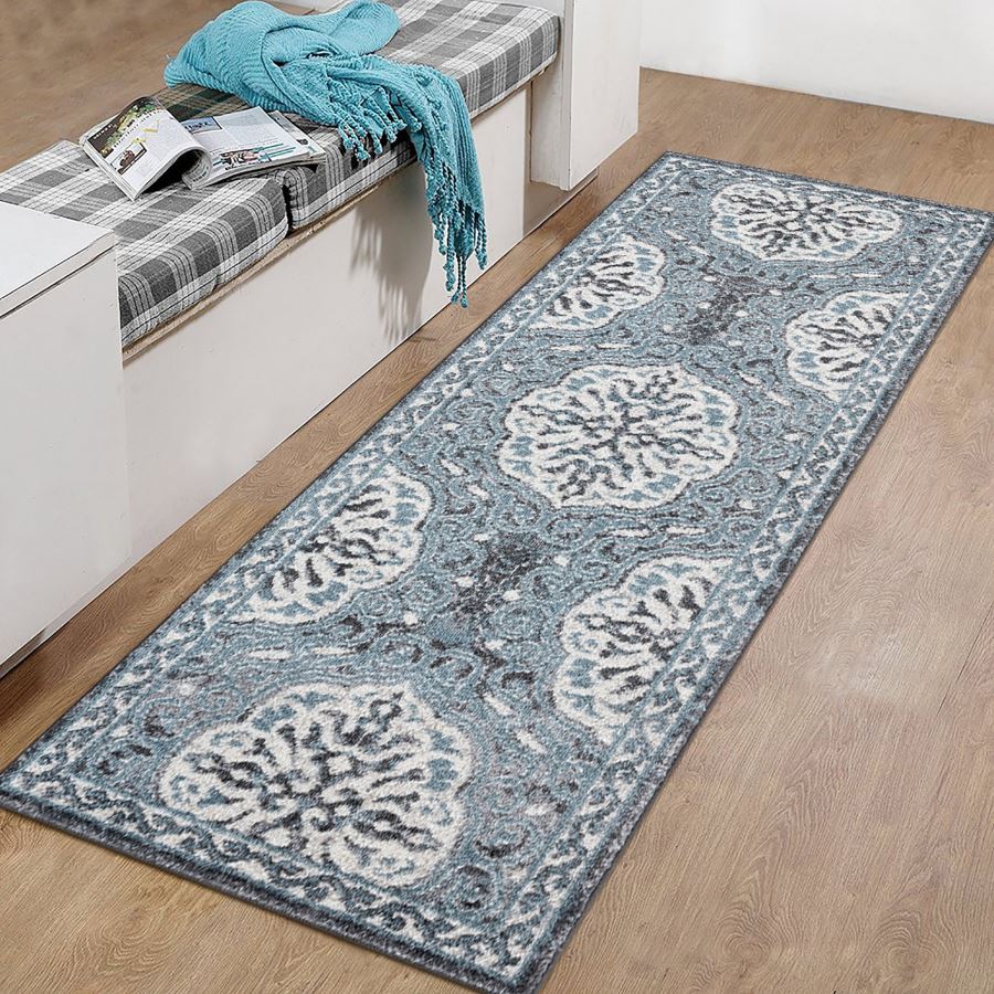Long blue patterned rug on a wooden floor with a bench and blue blanket in the background.