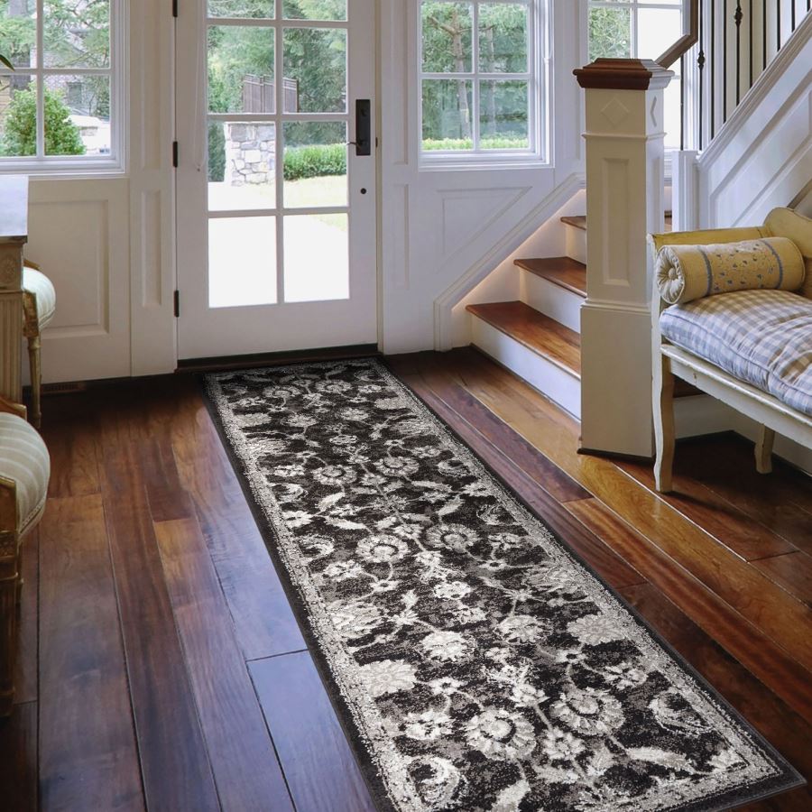 Long black and white patterned rug on a wooden floor in a home setting with a staircase and doors.
