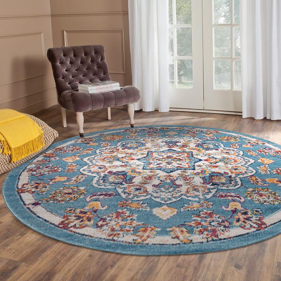 Round floral rug with colorful patterns on a wooden floor, with a chair and yellow blanket in the background.