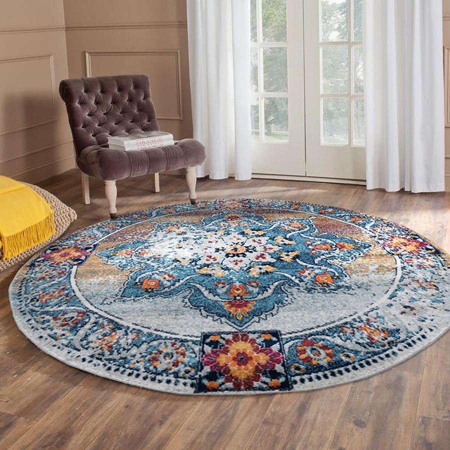 Round multicolored floral rug on a wooden floor with a chair and yellow pillow in the background.