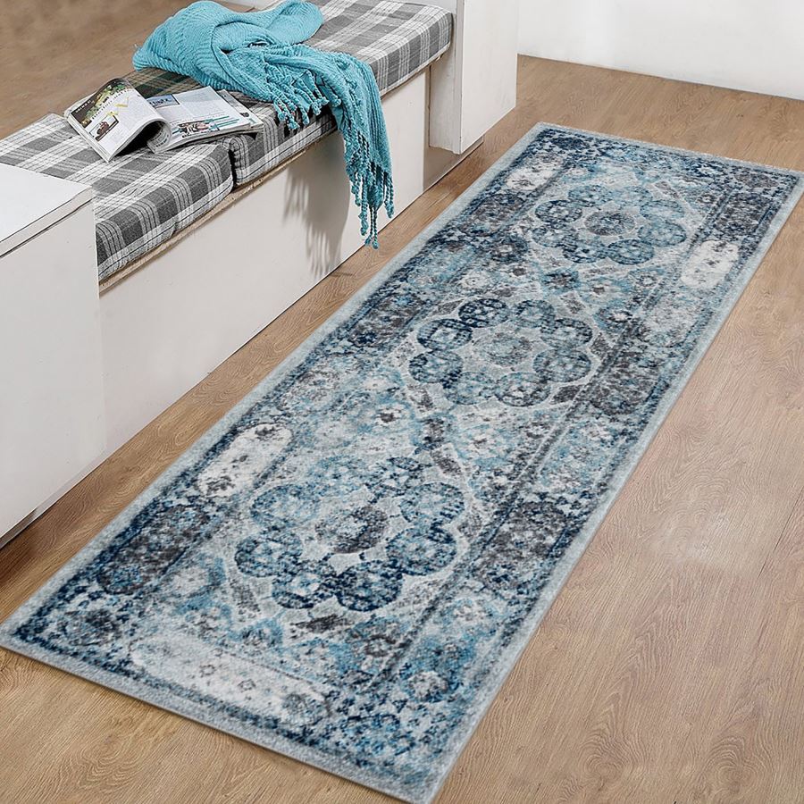 Long blue patterned rug on a wooden floor with a bench and blue blanket in the background.