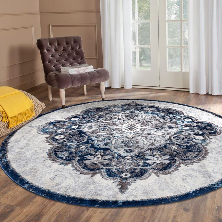 Round decorative rug with a blue and white pattern in a room with a chair and yellow blanket.