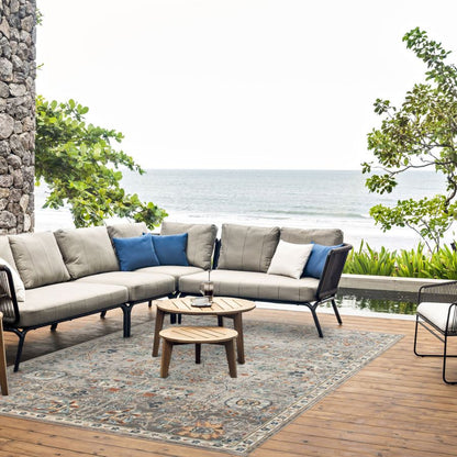 Outdoor patio set with sectional sofa, coffee tables, and cushions on a wooden deck with ocean view.