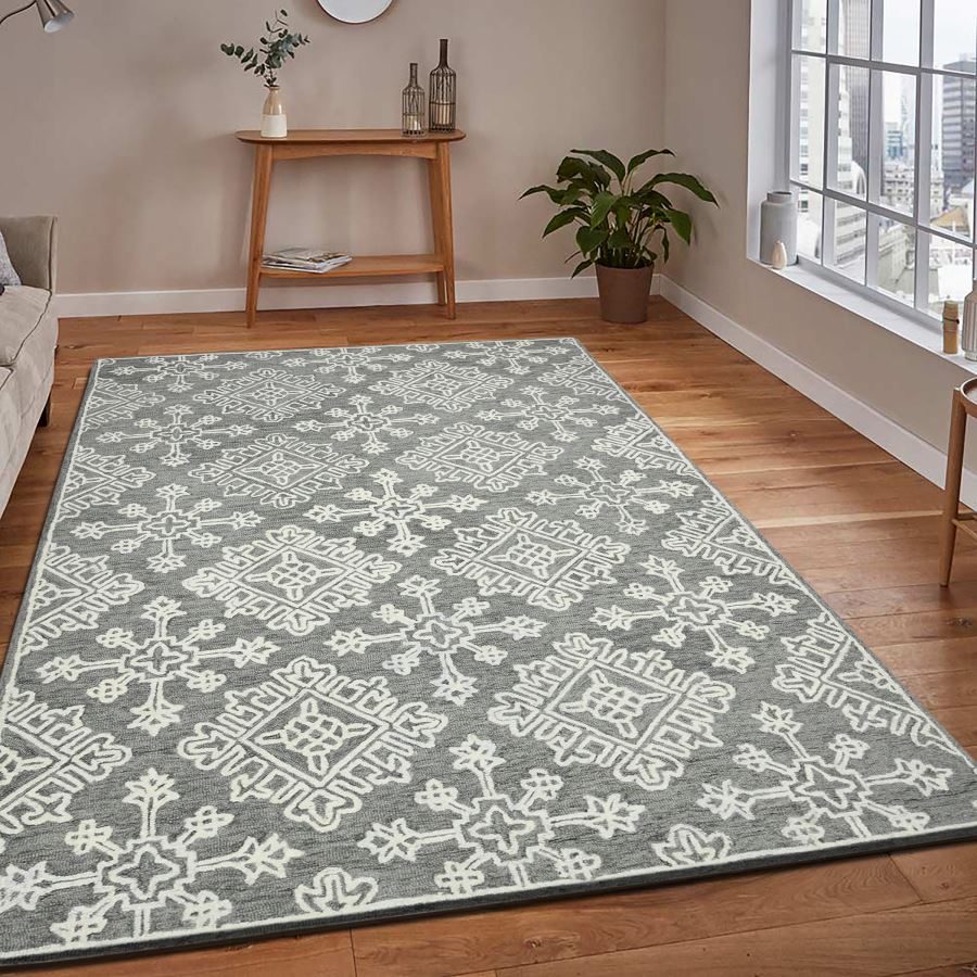 Gray and white patterned rug on a wooden floor with a side table and plant in the background.