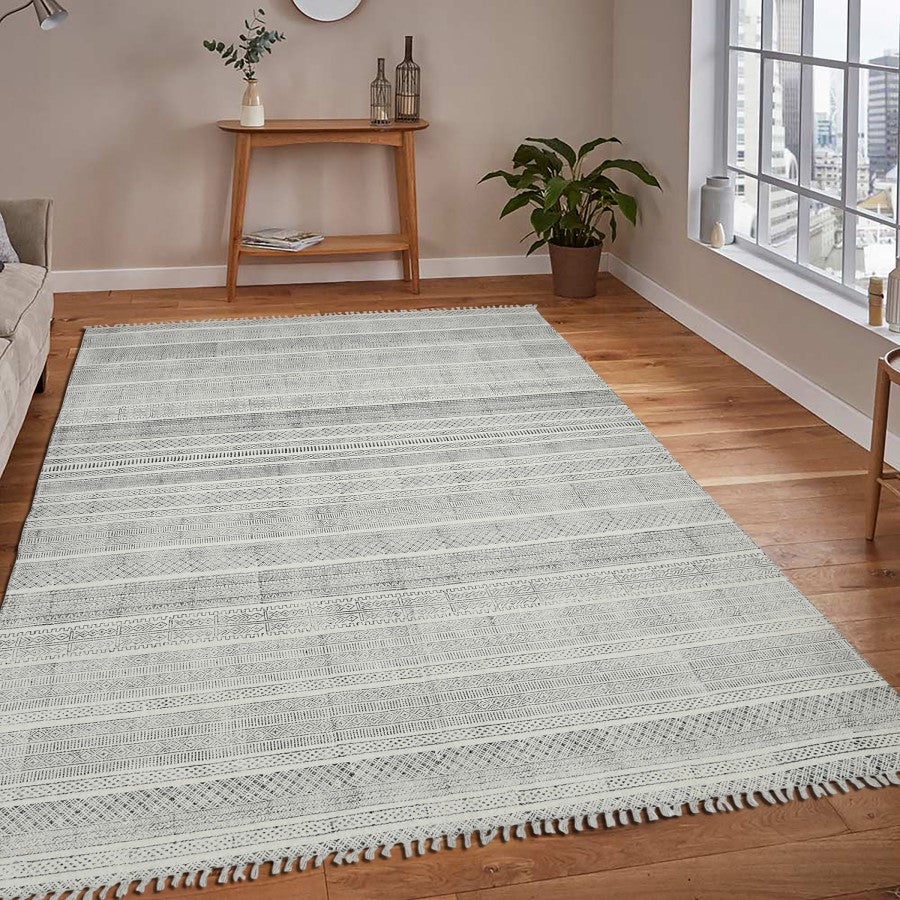 Gray area rug on a wooden floor in a living room setting with a window and small table.