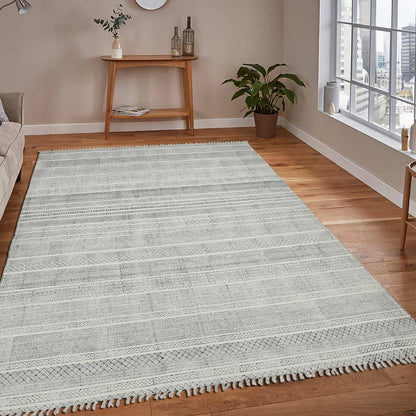 Gray area rug on a wooden floor in a living room setting with a window and small table.