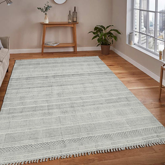 Gray area rug on a wooden floor in a living room setting with a window and small table.