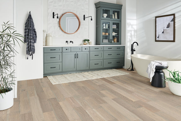 Modern bathroom with gray cabinets, freestanding bathtub, and wooden flooring.