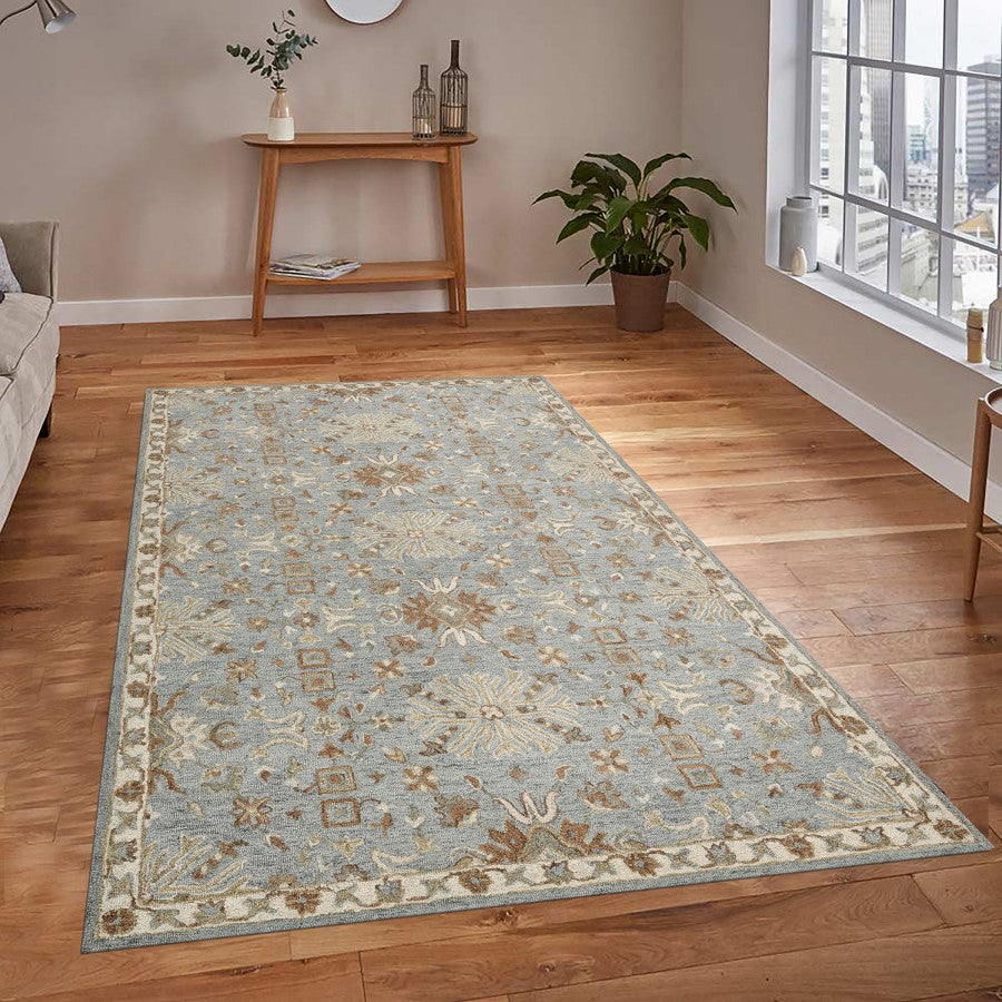 Decorative rug on a wooden floor with a side table and plants in the background.