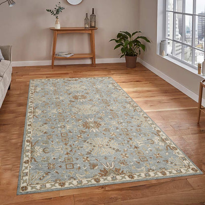Decorative rug on a wooden floor with a side table and plants in the background.