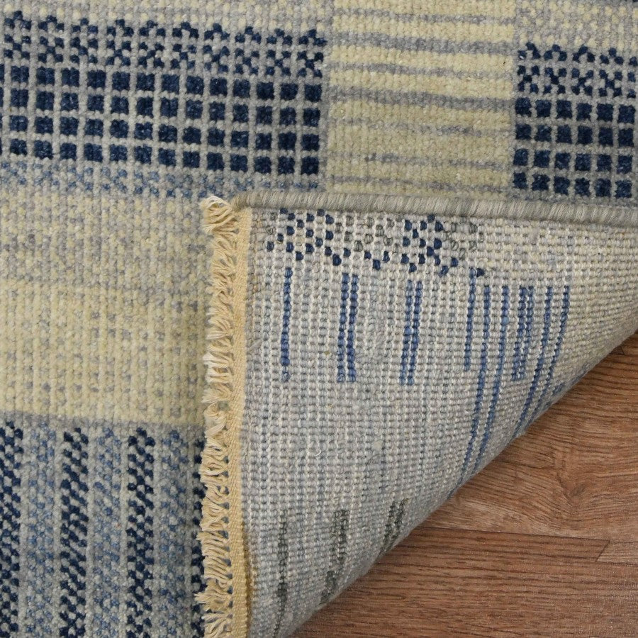 Close-up of a textured blue and beige rug on a wooden floor.