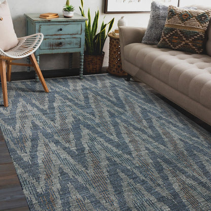Living room with a blue patterned rug, beige sofa, and wooden chair.