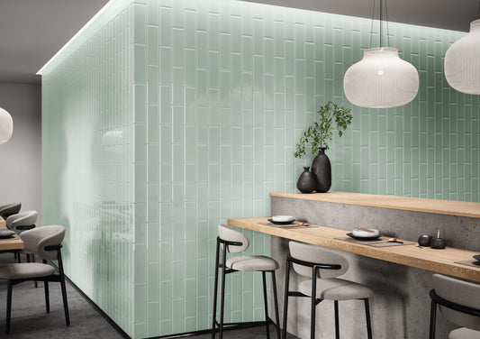 Modern restaurant interior with green tiled walls, wooden tables, and gray chairs.