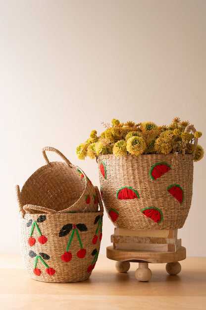 Two woven baskets, one with cherry design, one with watermelon design, on a wooden surface.