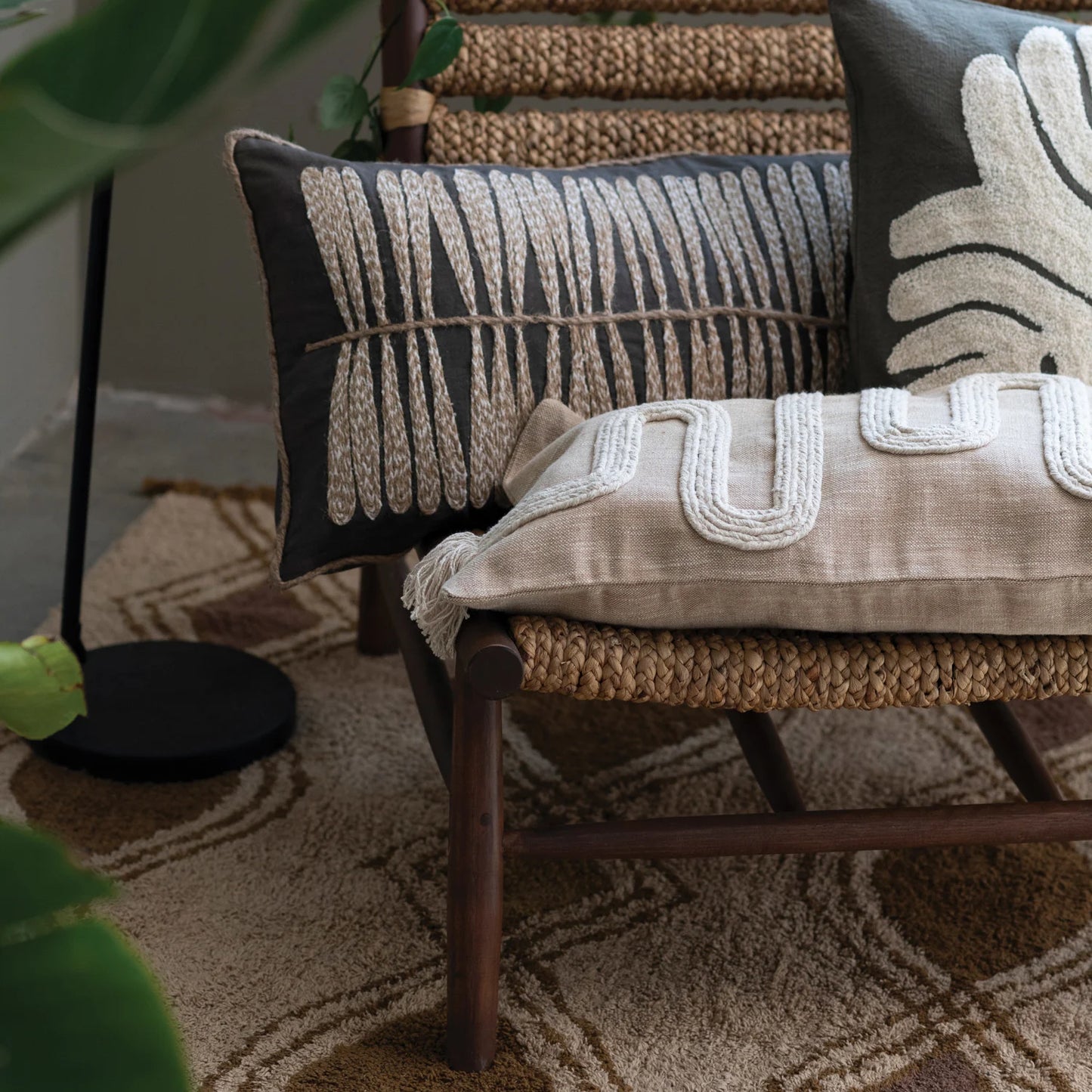 Decorative pillows on a chair with a patterned rug and plant in the background
