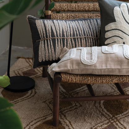 Decorative pillows on a chair with a patterned rug and plant in the background