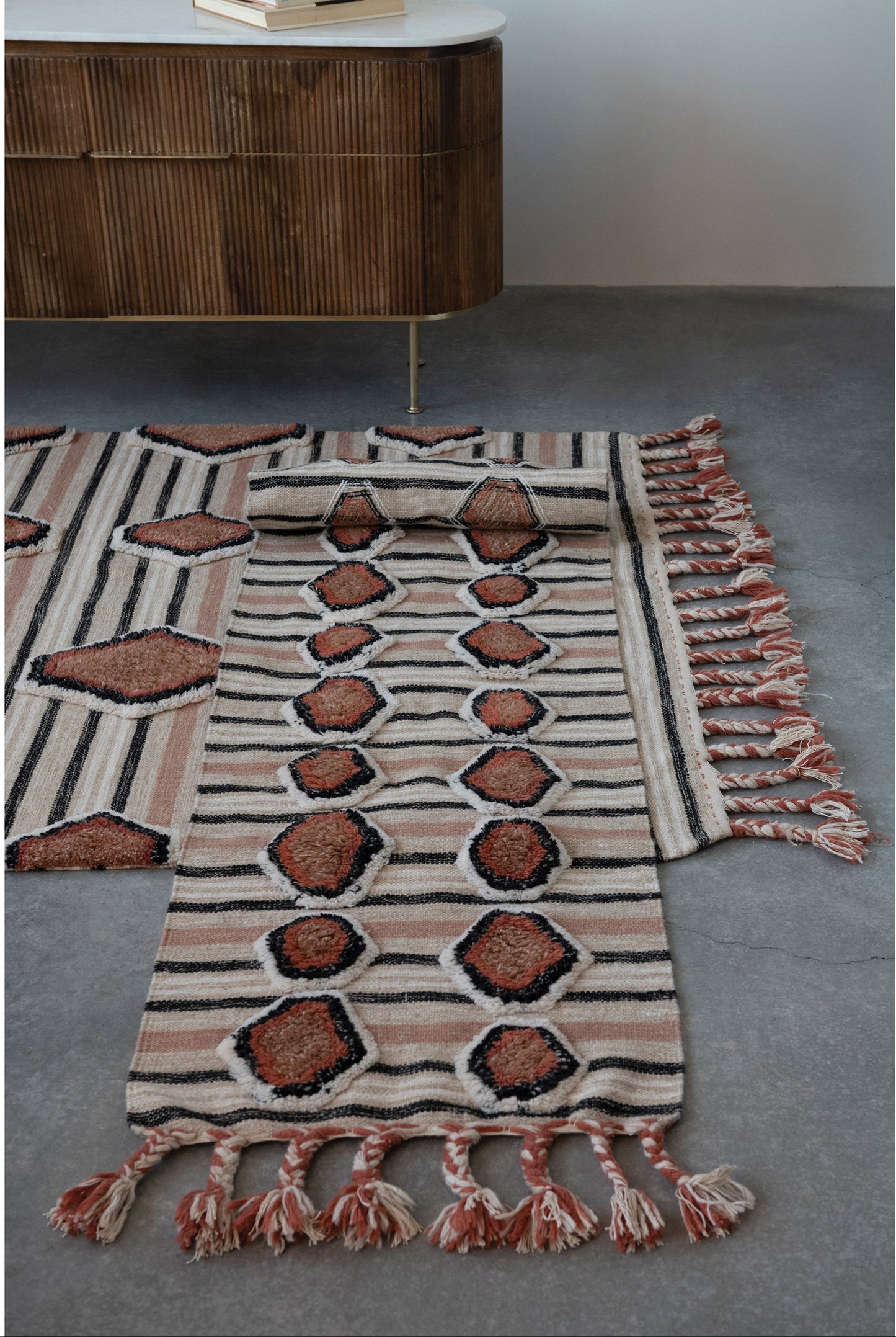 Decorative rug with geometric pattern and tassels on a concrete floor.