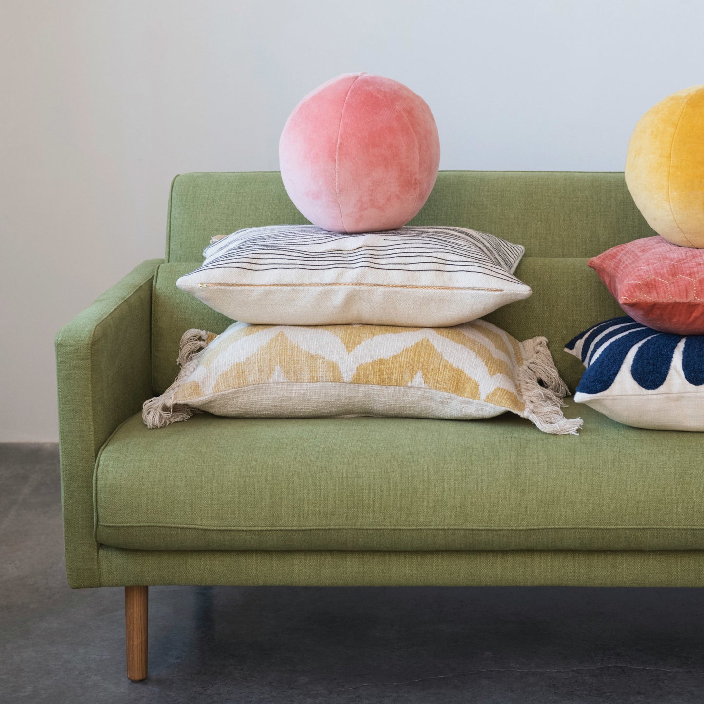 Green sofa with colorful pillows including a pink sphere pillow.