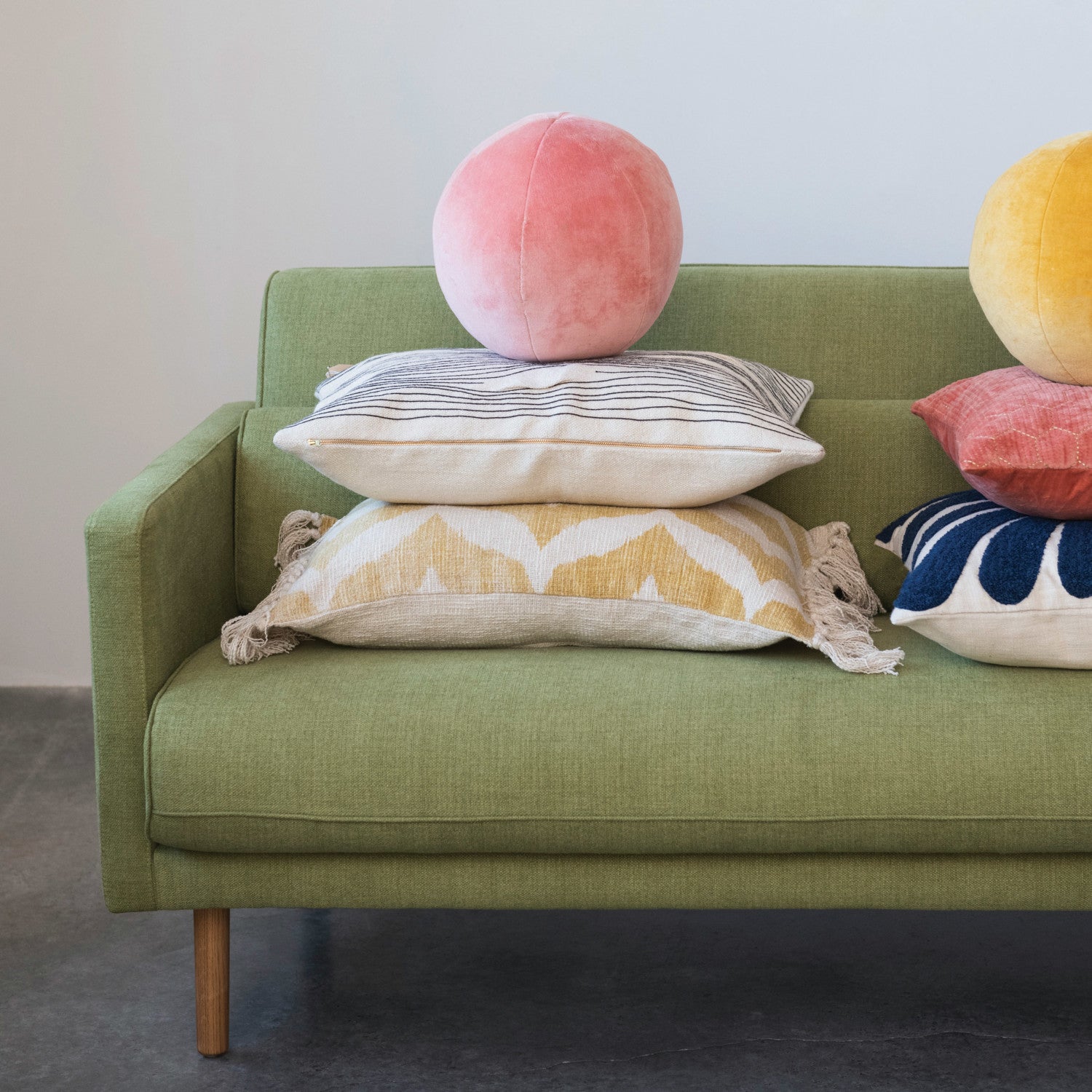 Green sofa with colorful pillows including a pink sphere pillow.