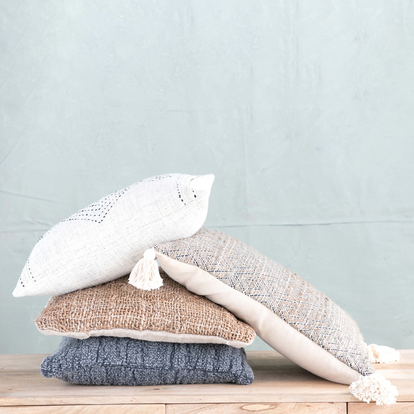 Stack of textured pillows on a wooden surface with a light blue background