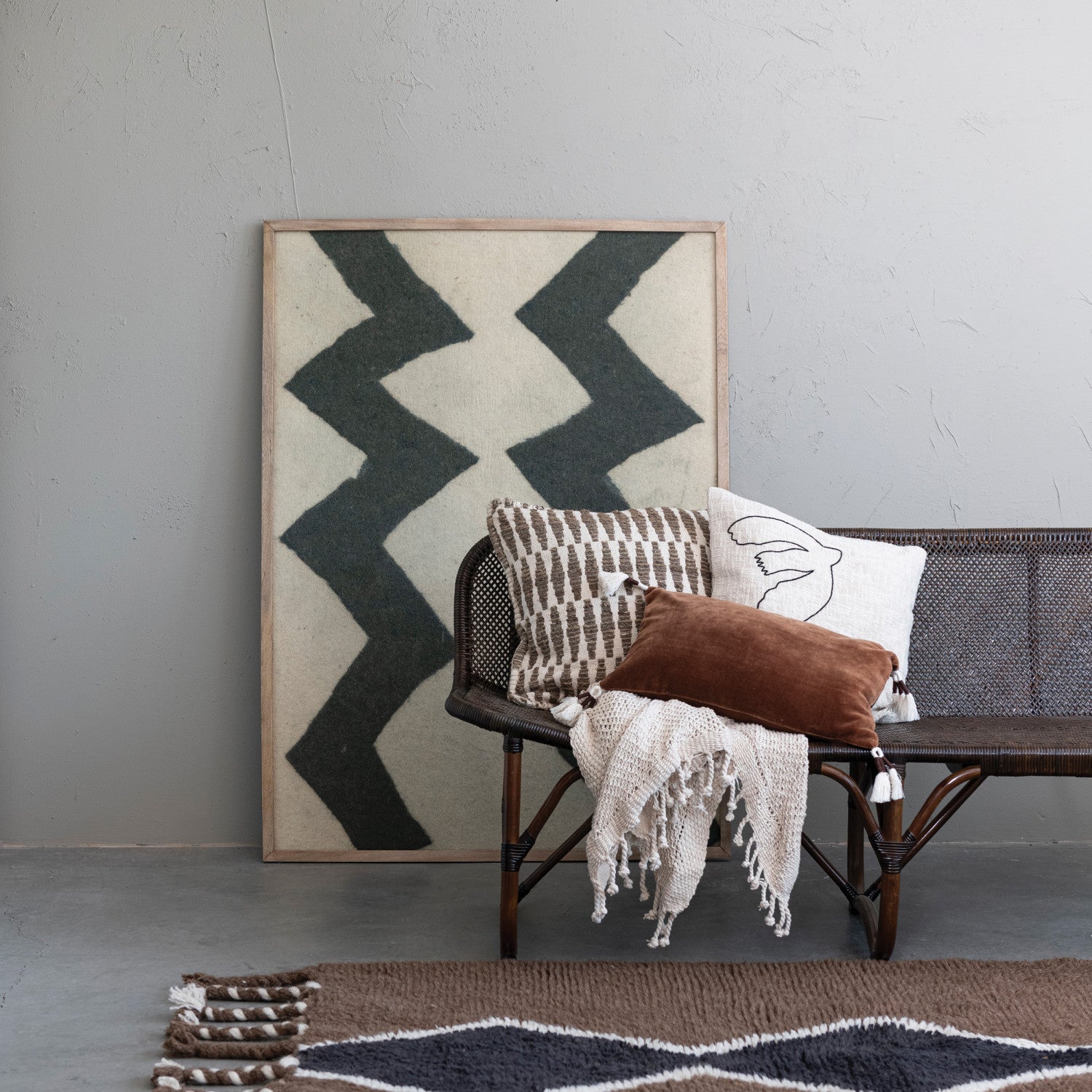 Wicker chair with decorative pillows and a blanket in front of a wall with a zigzag pattern.