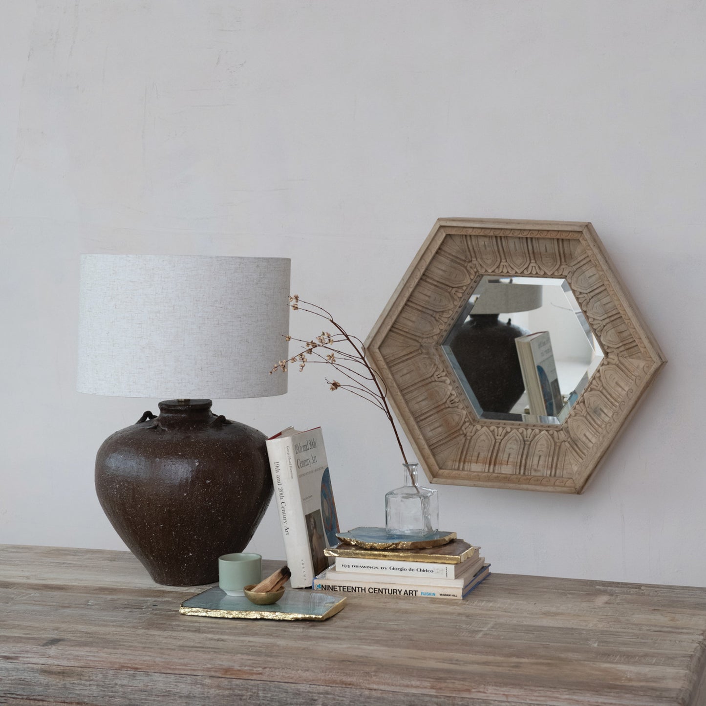 Decorative items on a wooden surface with a lamp, books, and a mirror.