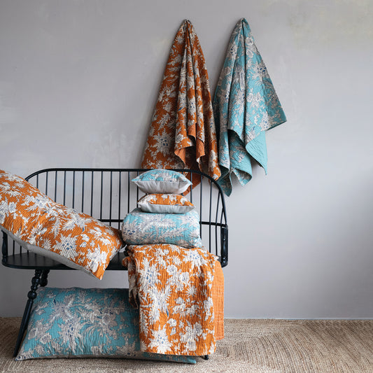 Decorative pillows and blankets with floral patterns on a black metal bench against a gray wall.