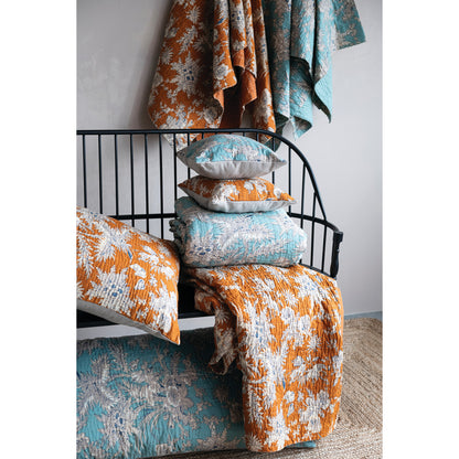 Bed with floral bedding and pillows in orange, blue, and white.