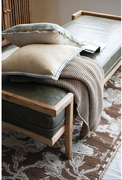 Wooden bench with cushions and a blanket on a patterned rug