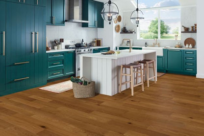 Modern kitchen with teal cabinets, white island, and wooden flooring.